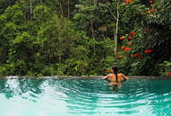 Woman bathing in an infinity pool surrounded by a lush tropical forest.
